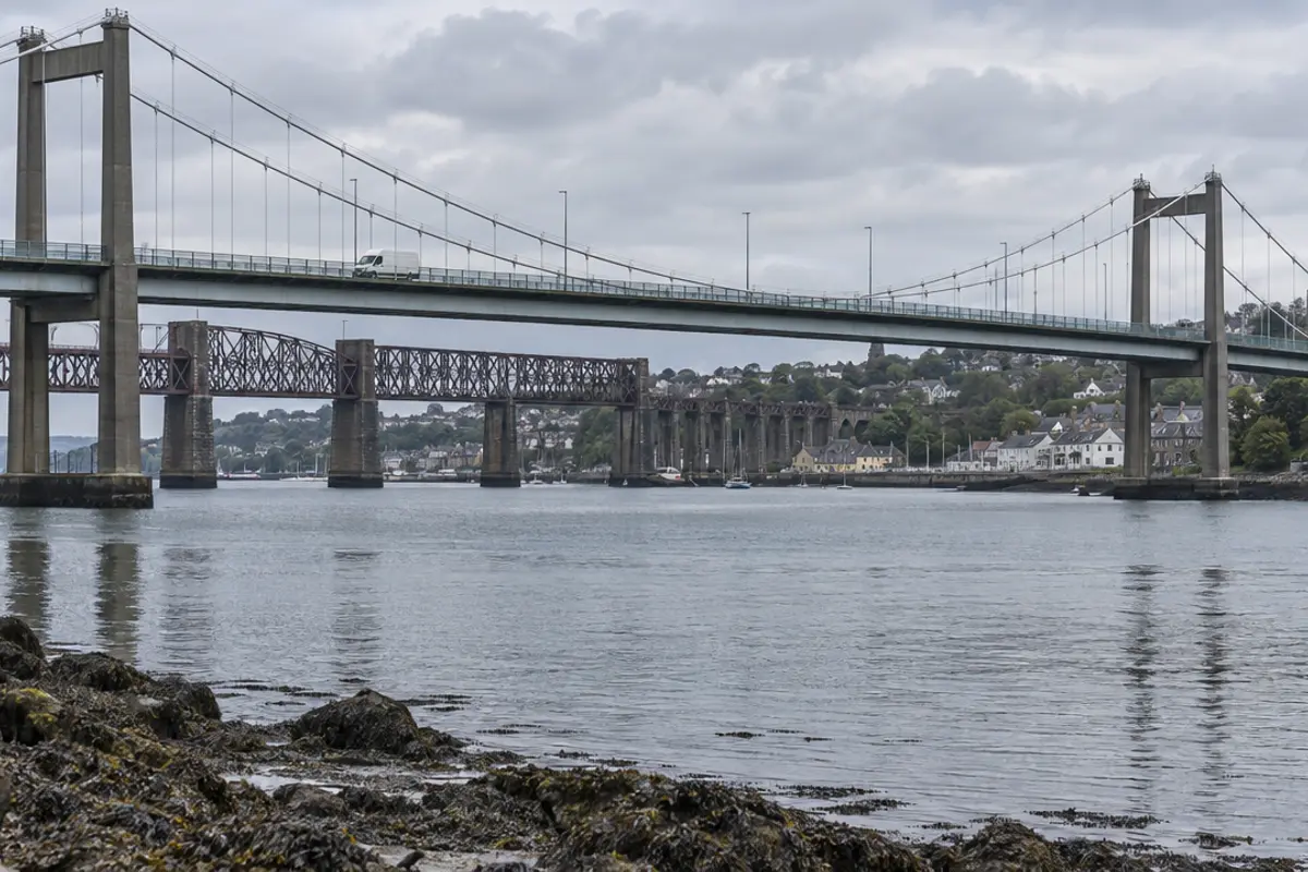 A suspension road bridge and an older railway bridge crossing a wide river estuary