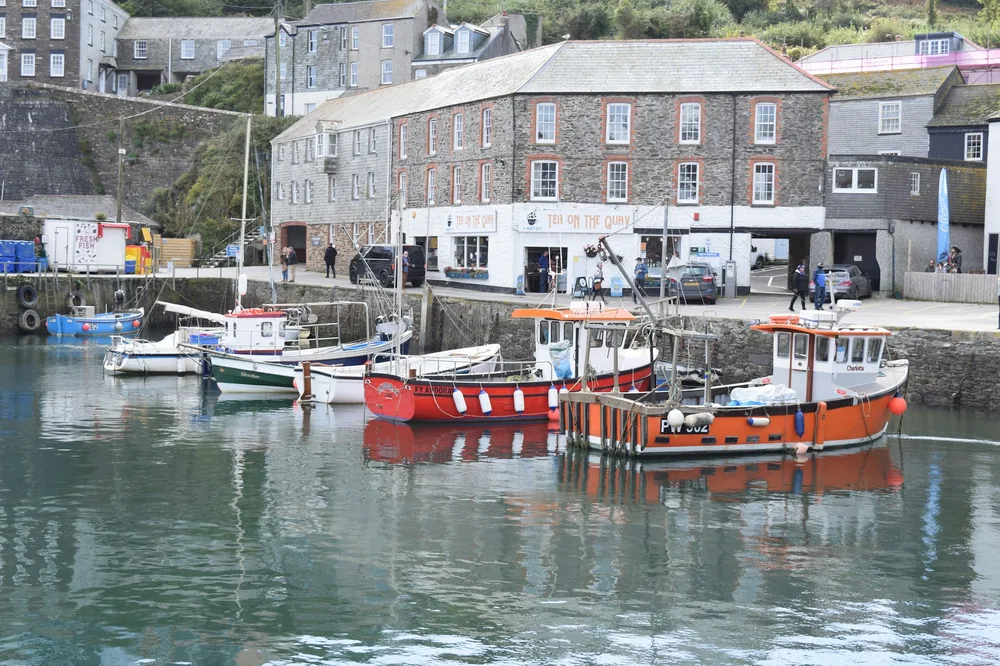 Fishing boats moored beside quayside buildings in Mevagissey Harbour, Cornwall.