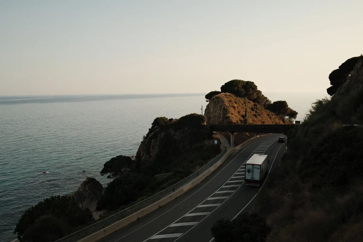 A freight lorry follows a coastal road beside the sea in Spain.