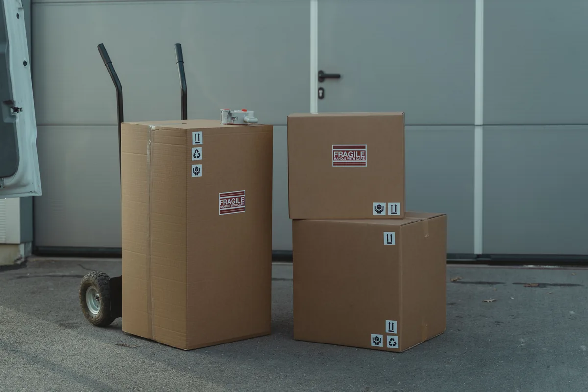 Three cardboard parcels beside a hand trolley outside a loading entrance.