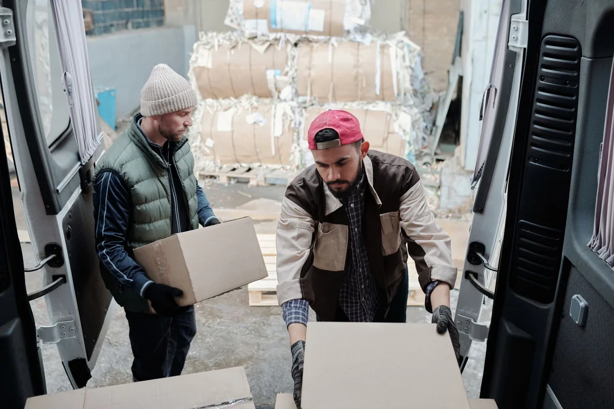 Two people handling cartons at the rear doors of a van.