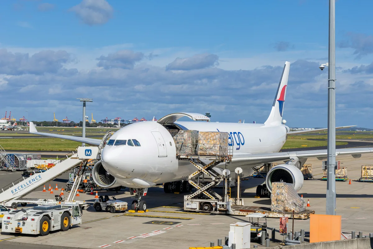 Wrapped cargo on a raised loader beside an open cargo aircraft at Sydney Airport.
